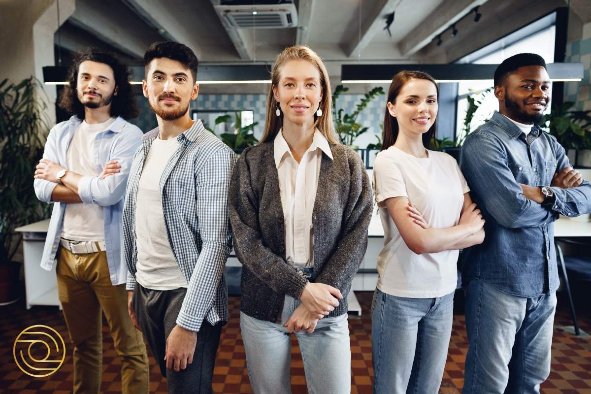 A diverse group of five young professionals standing confidently in an office, arms crossed, showcasing teamwork and individual strengths.