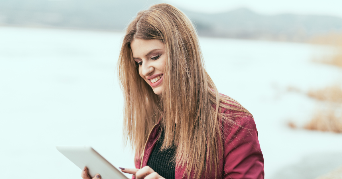 A smiling woman outdoors using a tablet; researching the tax advantages of LLC business.