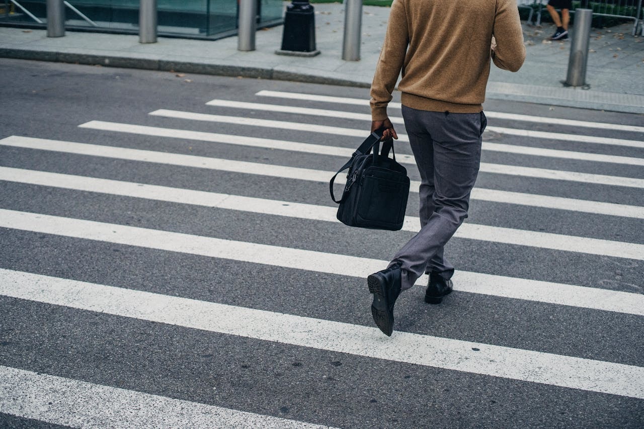 Person crossing a street at a crosswalk, walking with a bag in an urban setting