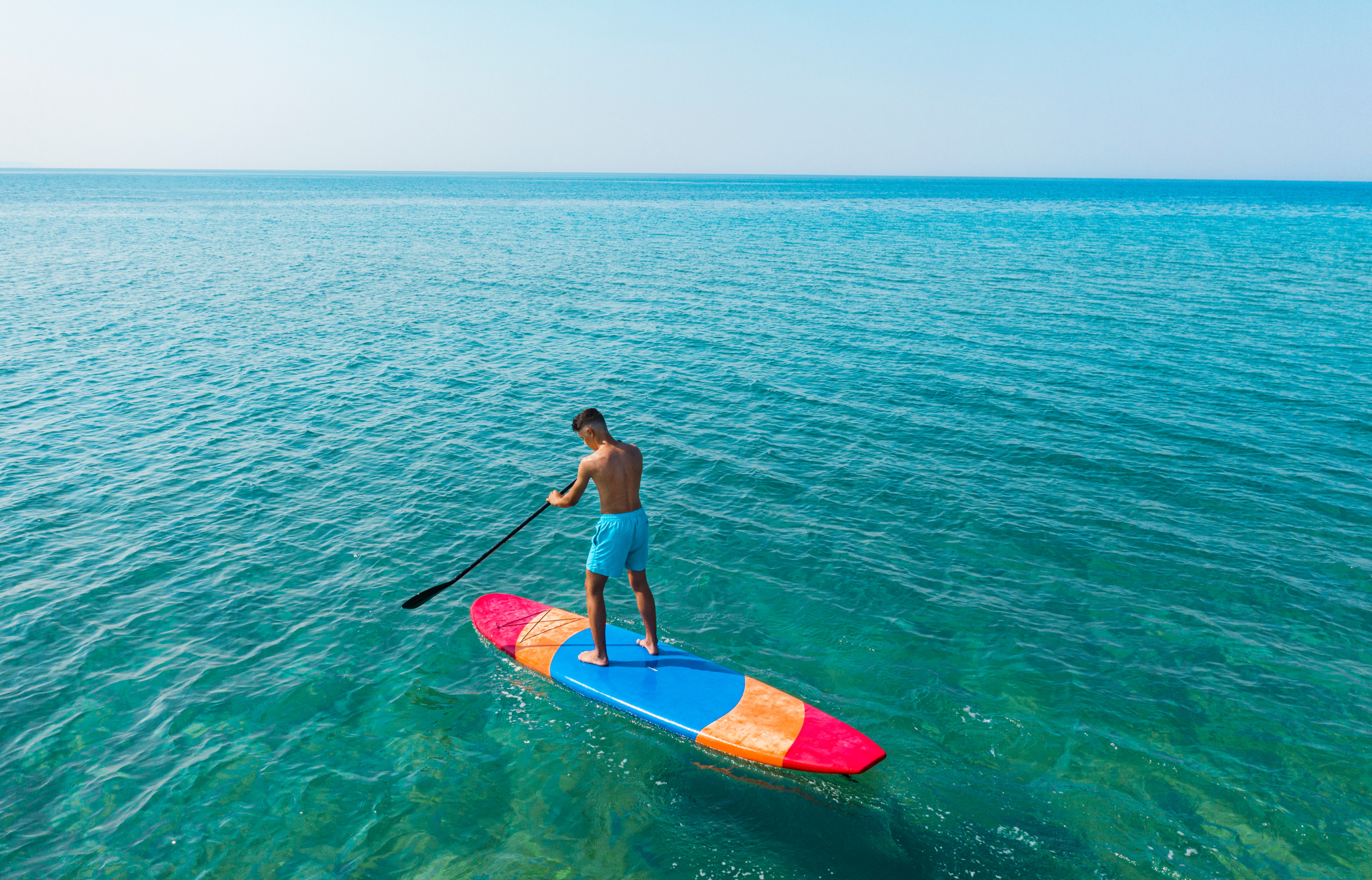 Man stand up paddle boarding in beautiful blue-green calm water - Adventure Wise Travel Gear