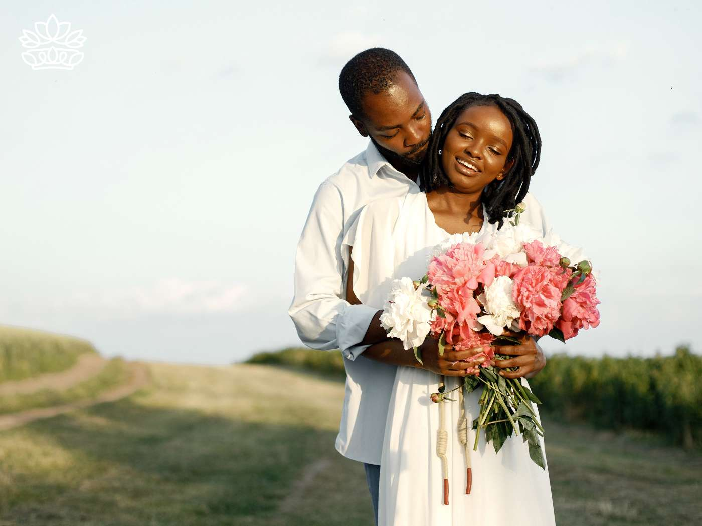 A loving couple shares an intimate moment in a serene field, the woman holding a lush bouquet from the Engagement Flowers Collection, a testament to their shared journey ahead, brought to you by Fabulous Flowers and Gifts.