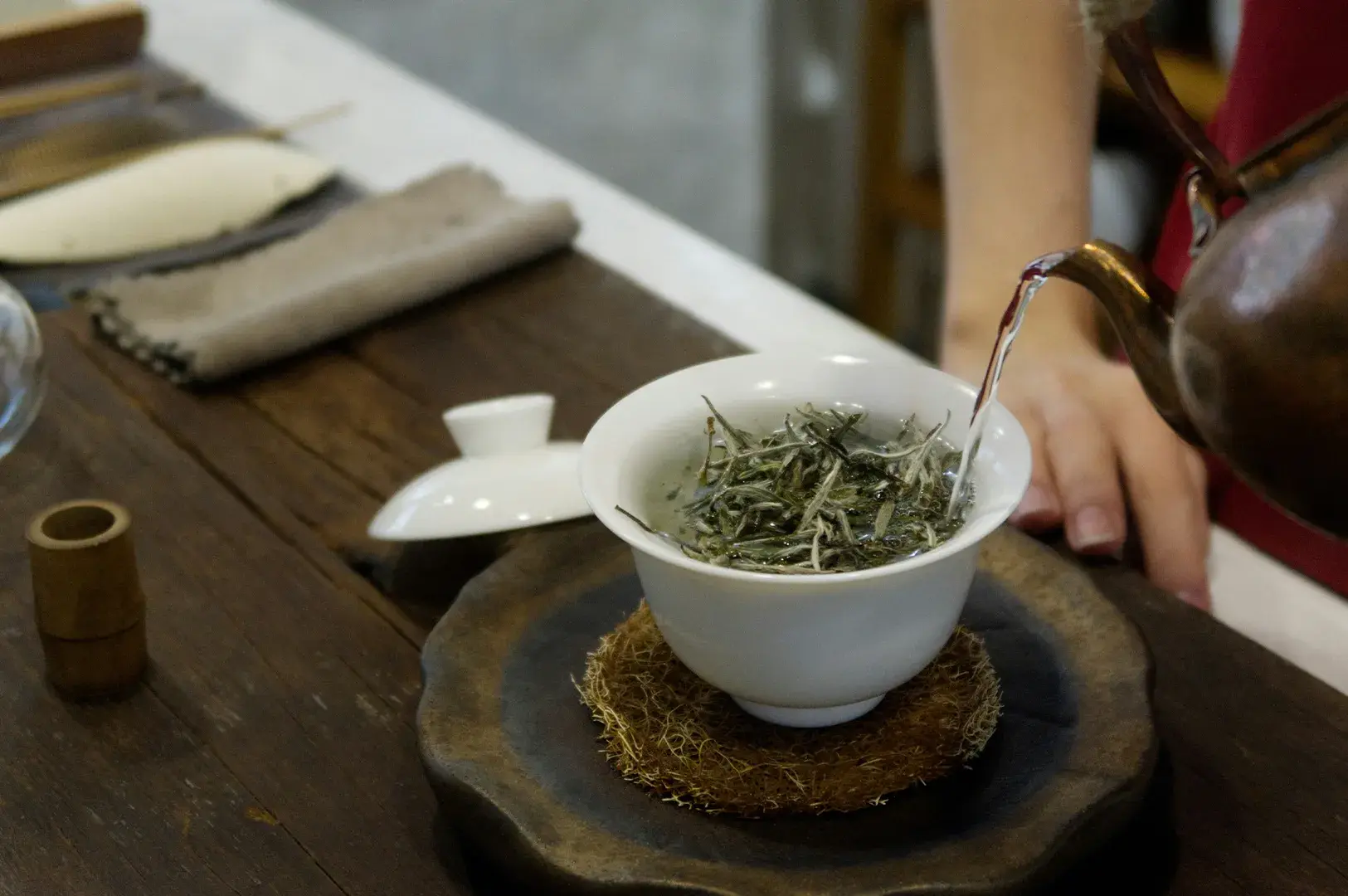 Hot water poured into a ceramic gaiwan with loose tea leaves.