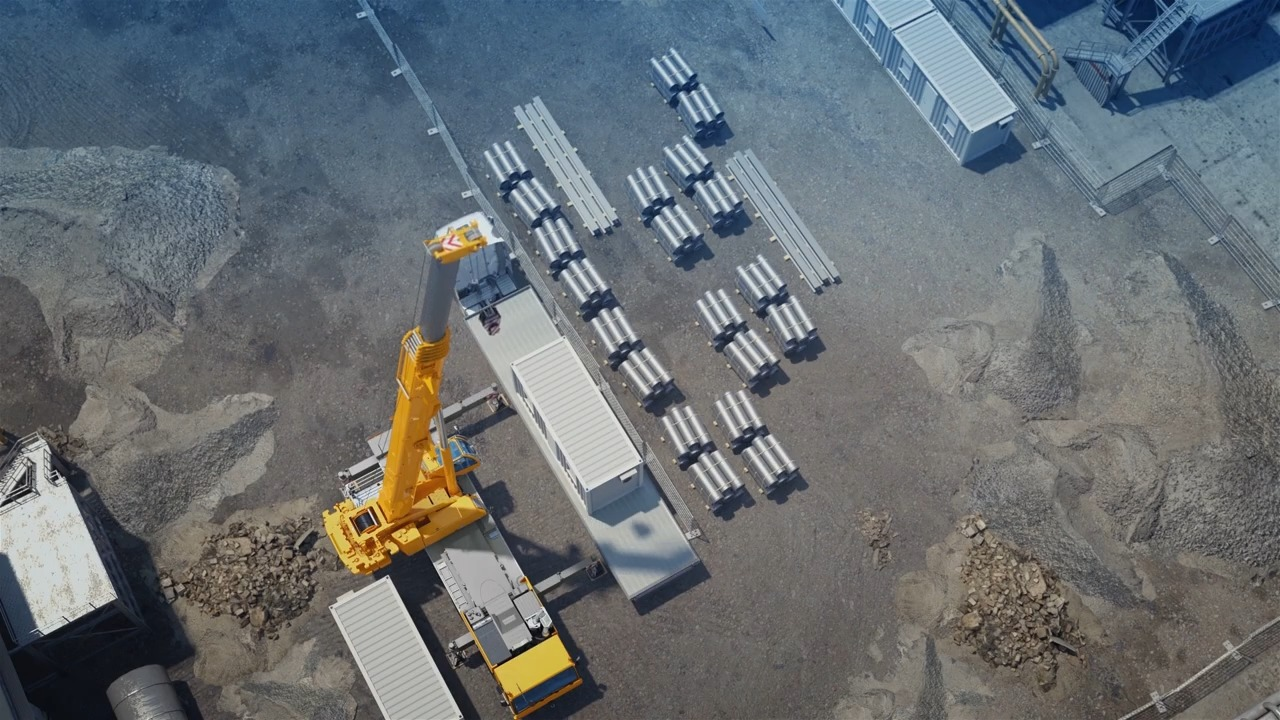 Aerial view of a construction site with a yellow crane, metal beams, and equipment on a gravel surface, emphasizing industrial development and heavy machinery usage