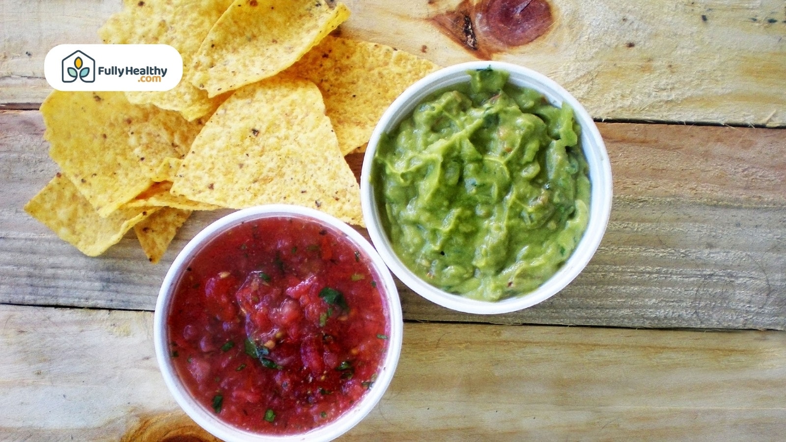 Tortilla chips with salsa and guacamole on a wooden table.