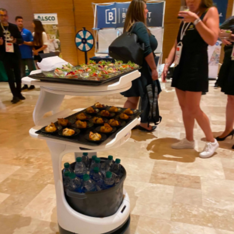 A photograph of the Servi service robot transporting food and beverages at an event.