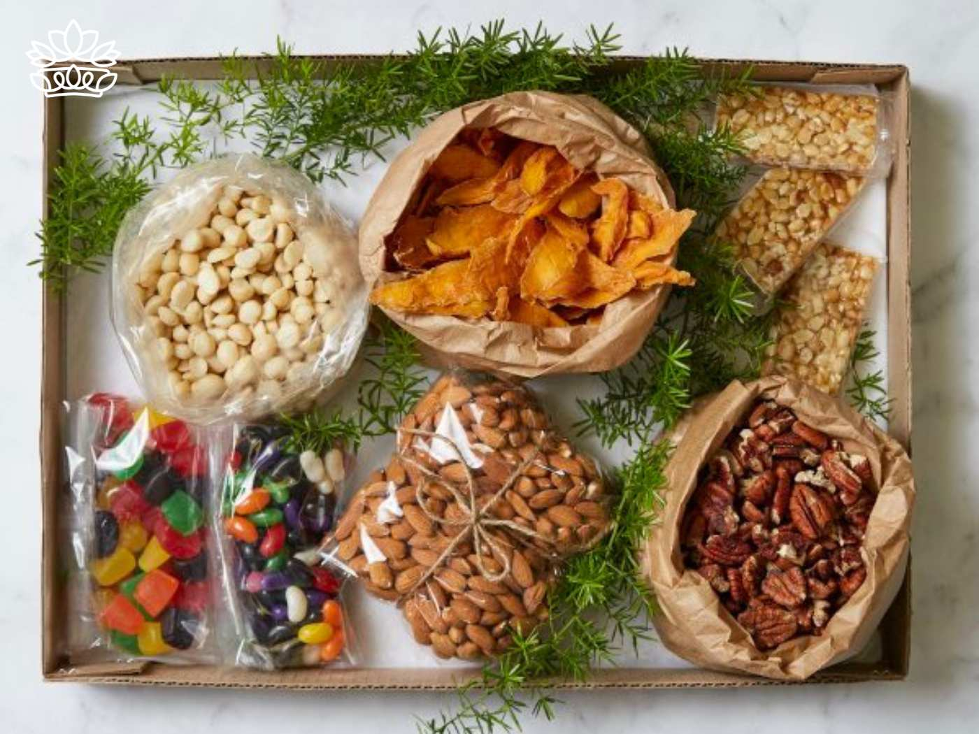 A selection of snacks, including dried mango slices, macadamia nuts, almonds, pecans, jelly beans, and seed bars, arranged in an eco-friendly box with greenery. Fabulous Flowers and Gifts. Gifts for Him. Delivered with Heart.