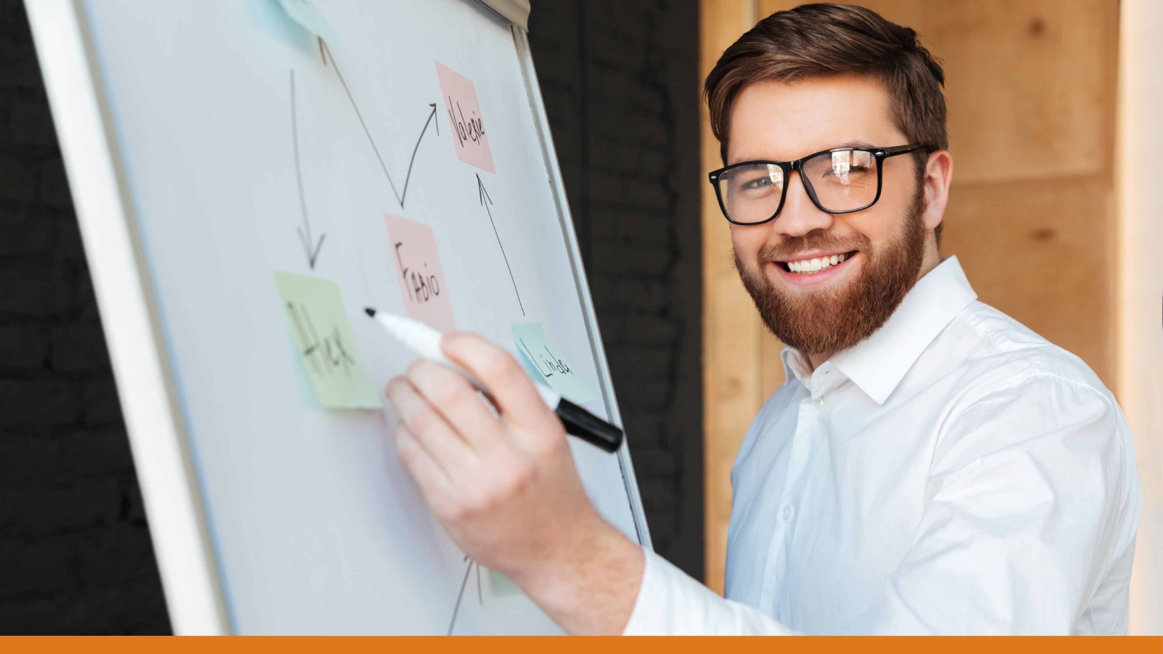 Man smiling while drawing a flowchart on a whiteboard, symbolizing strategies to send alerts to local authorities and mobile devices during critical situations.