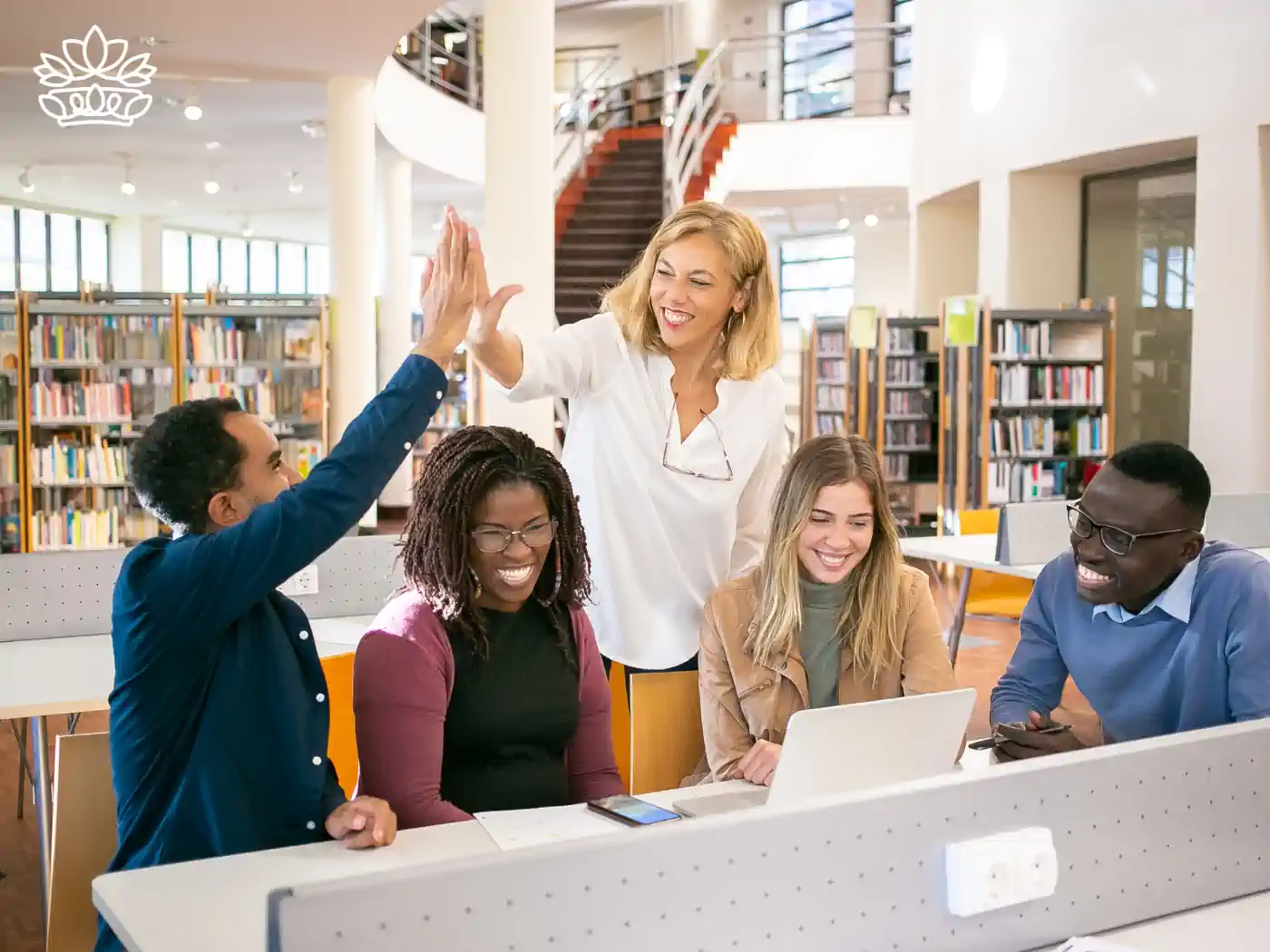 Enthusiastic adult education teacher celebrating success with a diverse group of students in a library, exemplifying inclusive and supportive learning, delivered with heart by Fabulous Flowers and Gifts.