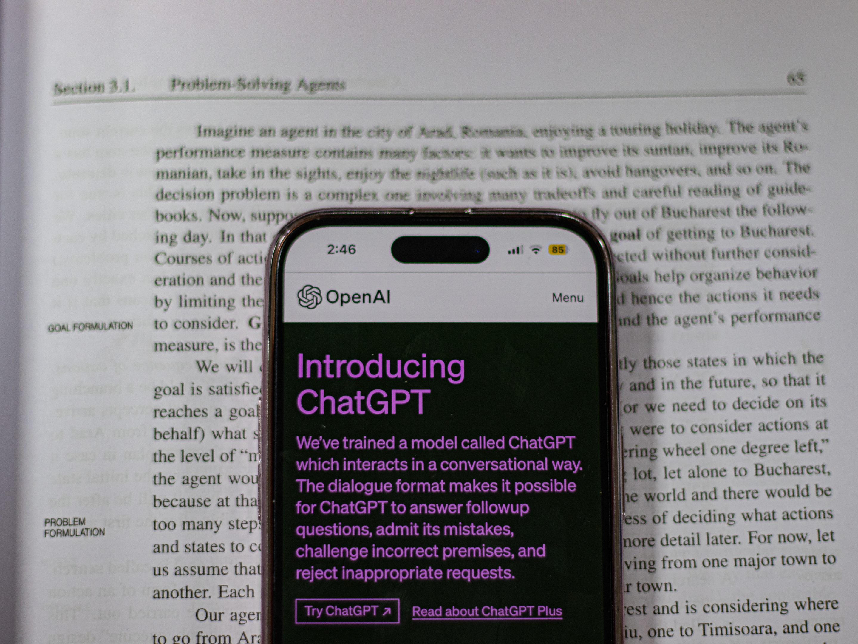 An open textbook with a phone on it. The phone shows a ChatGPT webpage.