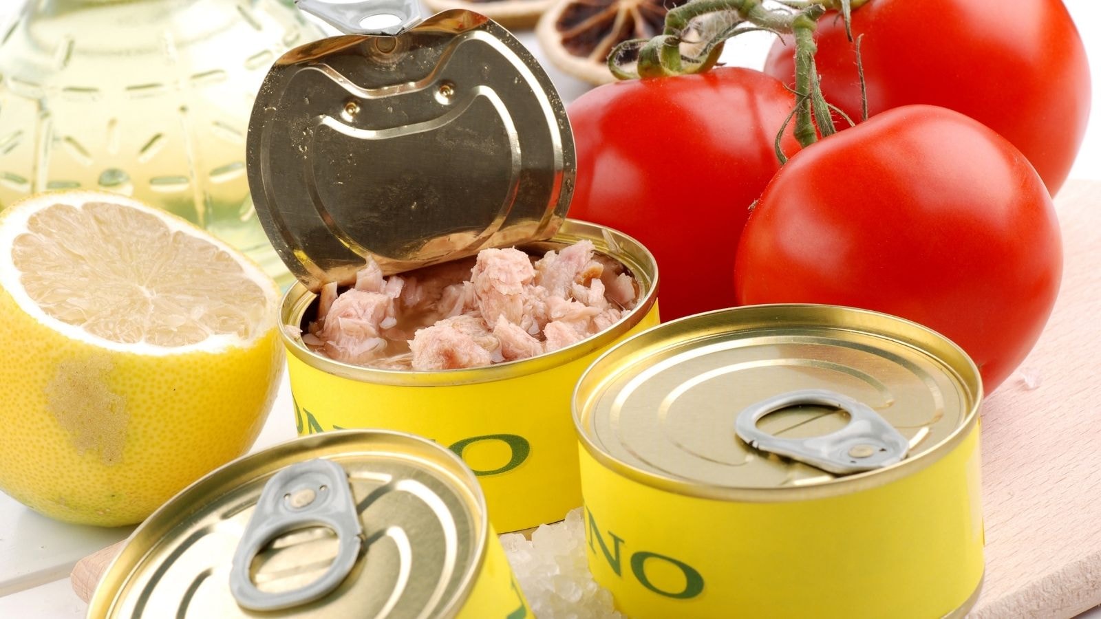 Canned tuna opened beside tomatoes, lemon, and olive oil on a kitchen counter