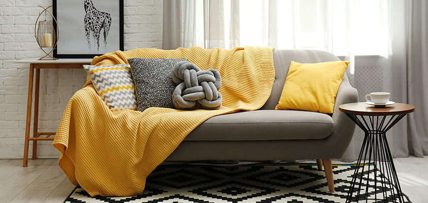 These yellow and grey throw pillows and blankets bring a pop of colour to the grey couch, providing visual interest and tying together the room's colour scheme.