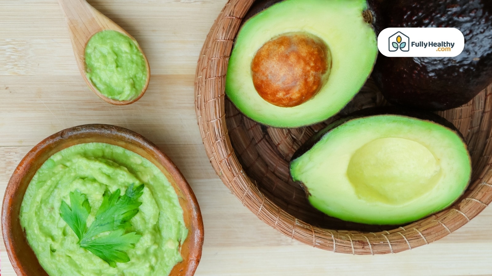 Wooden bowl of guacamole with parsley and halved avocados beside