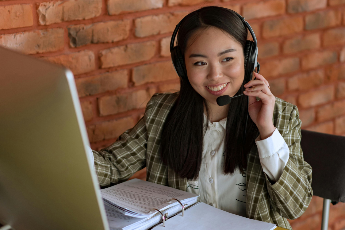 Smiling Filipino virtual assistant wearing a headset during an online support call at her workstation