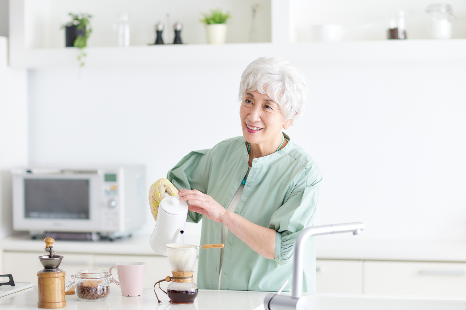 Elderly woman pouring tea in a bright kitchen.