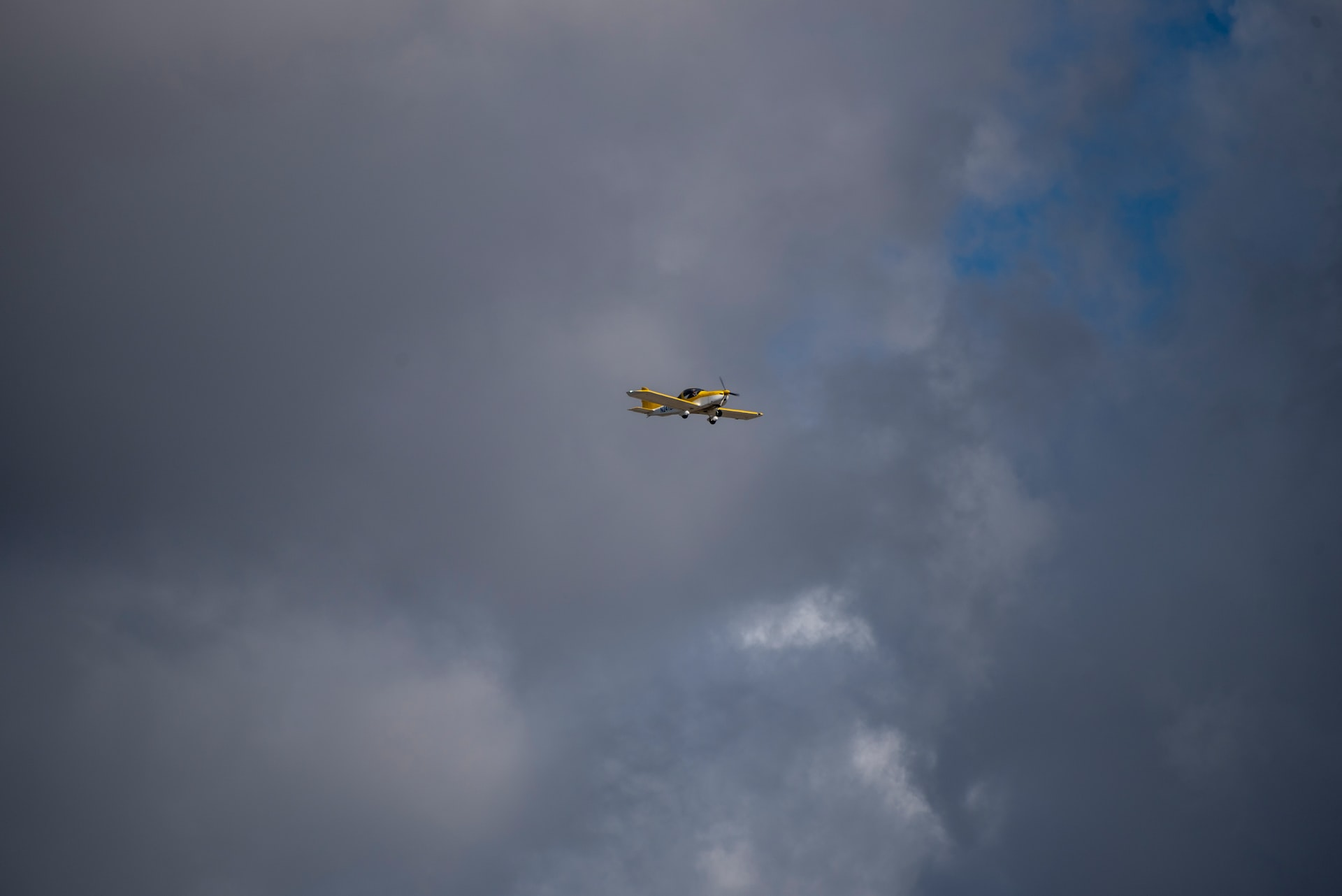 A small airplane flying under some dark clouds.