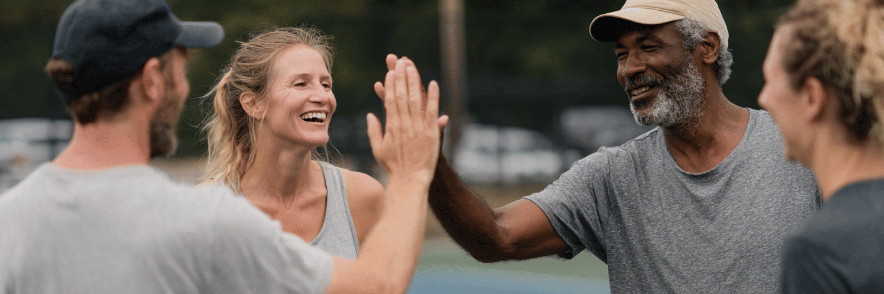 Four pickleball players high‑fiving and chatting at the net on an outdoor court.