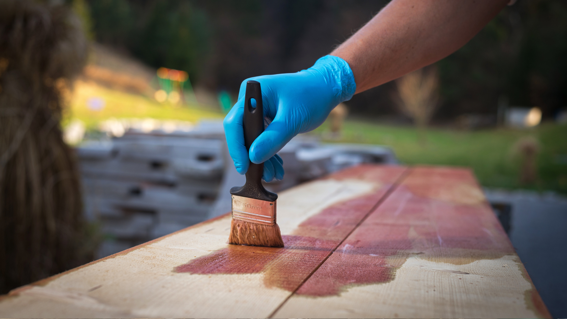 A hand applying a coat of stain to pine wood with a paint brush.