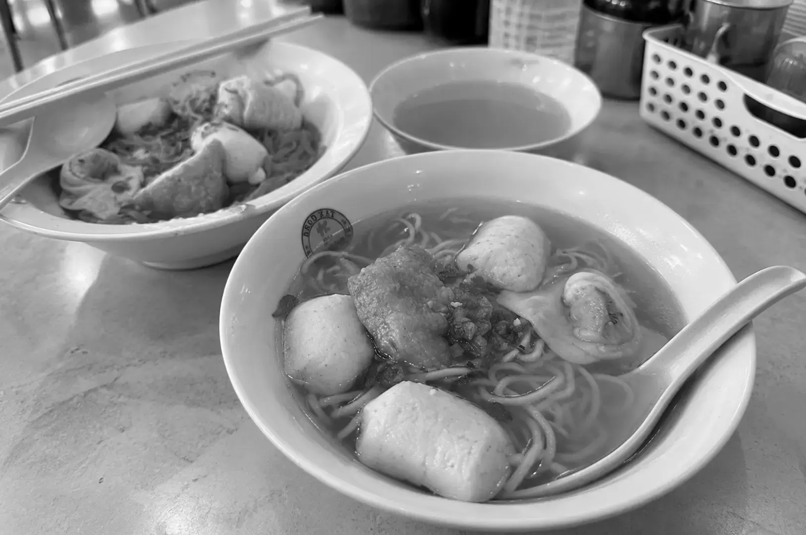 A simple hawker-style bowl of fishball noodles, featuring round fishballs and noodles in a clear, light broth.