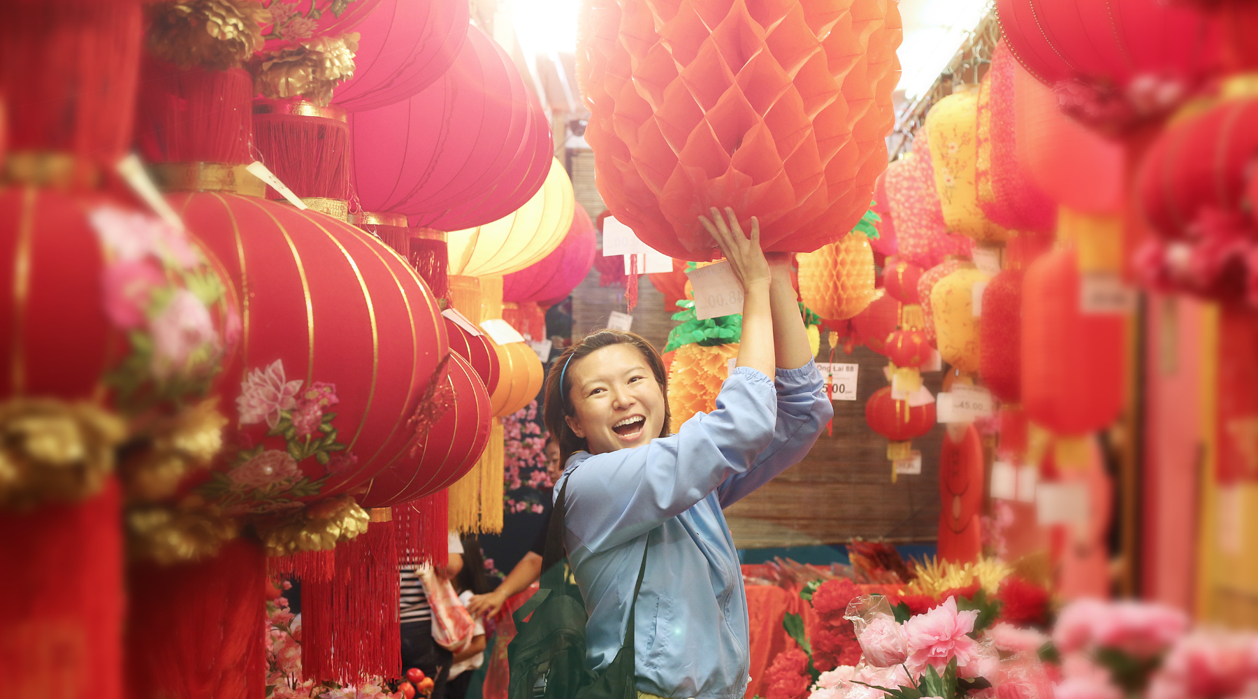 Joyful woman reaching for a bright orange lantern at a vibrant Lunar New Year market