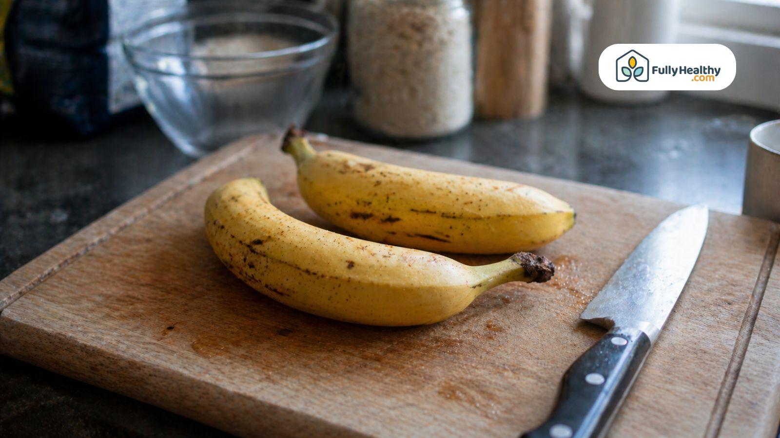 Two ripe bananas on a cutting board next to a kitchen knife in a home kitchen setting.