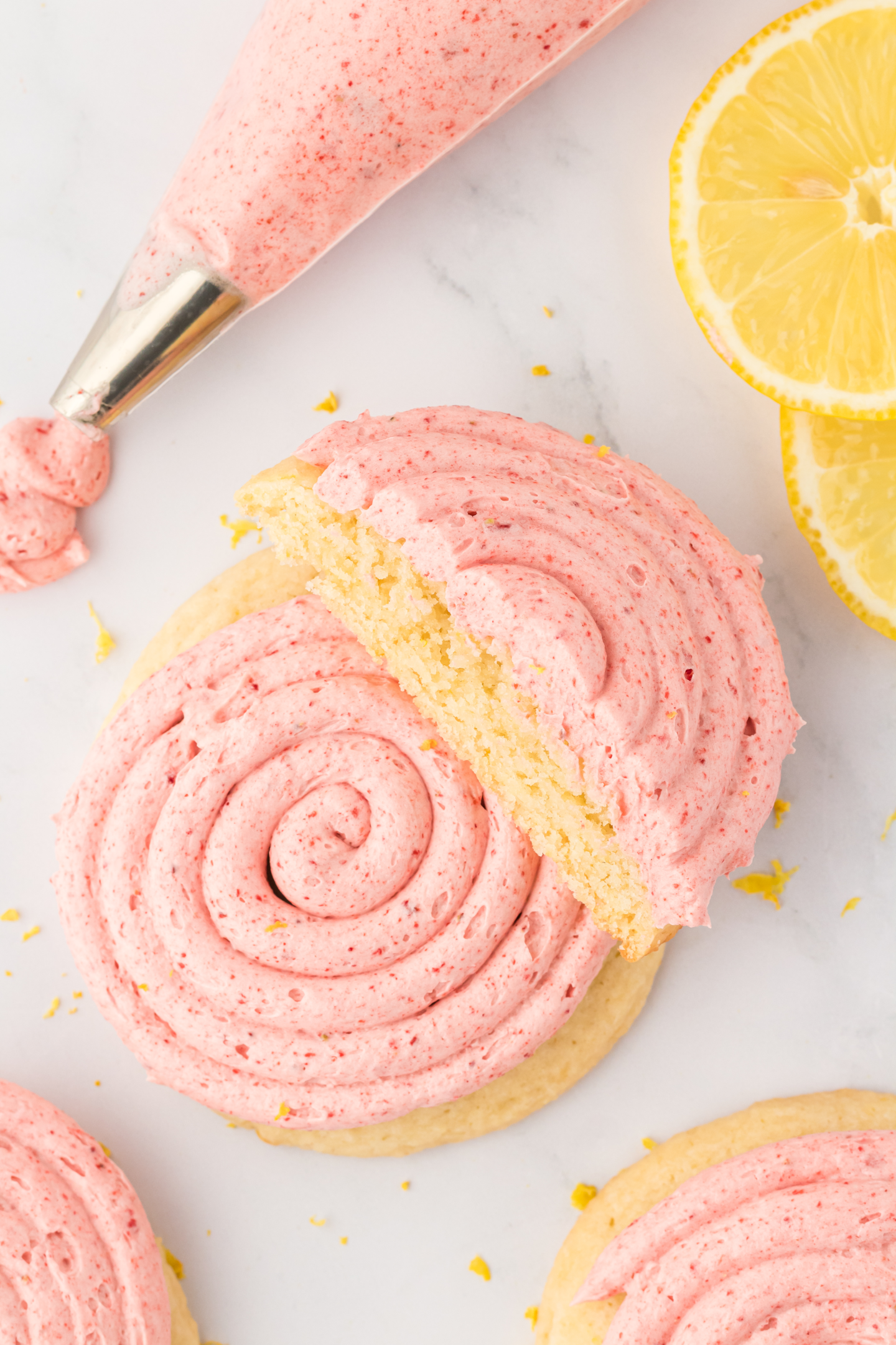 two strawberry lemonade cookies and a piping bag of strawberry buttercream frosting