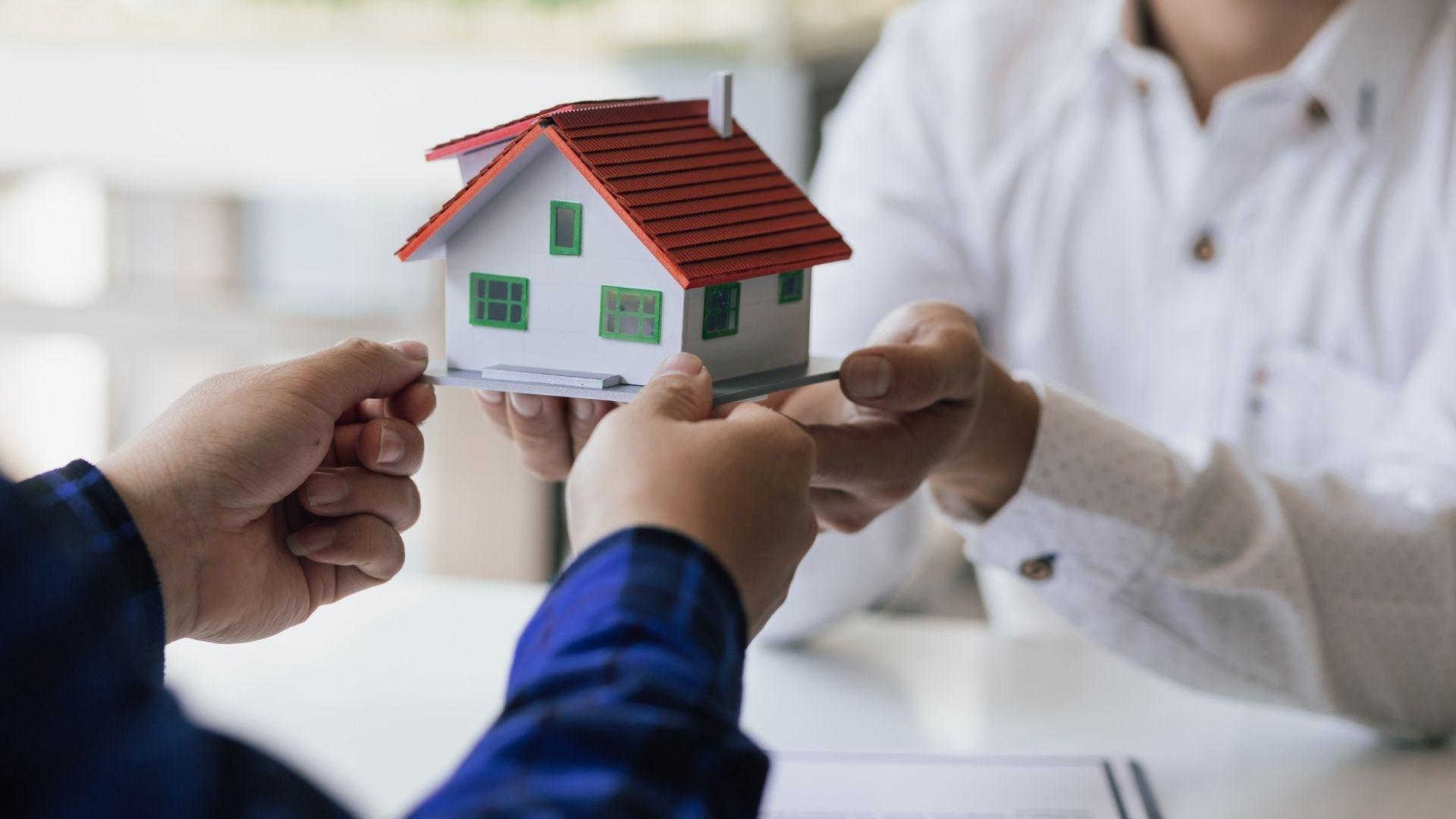 Hands exchanging a model house during a real estate or property inheritance transaction.