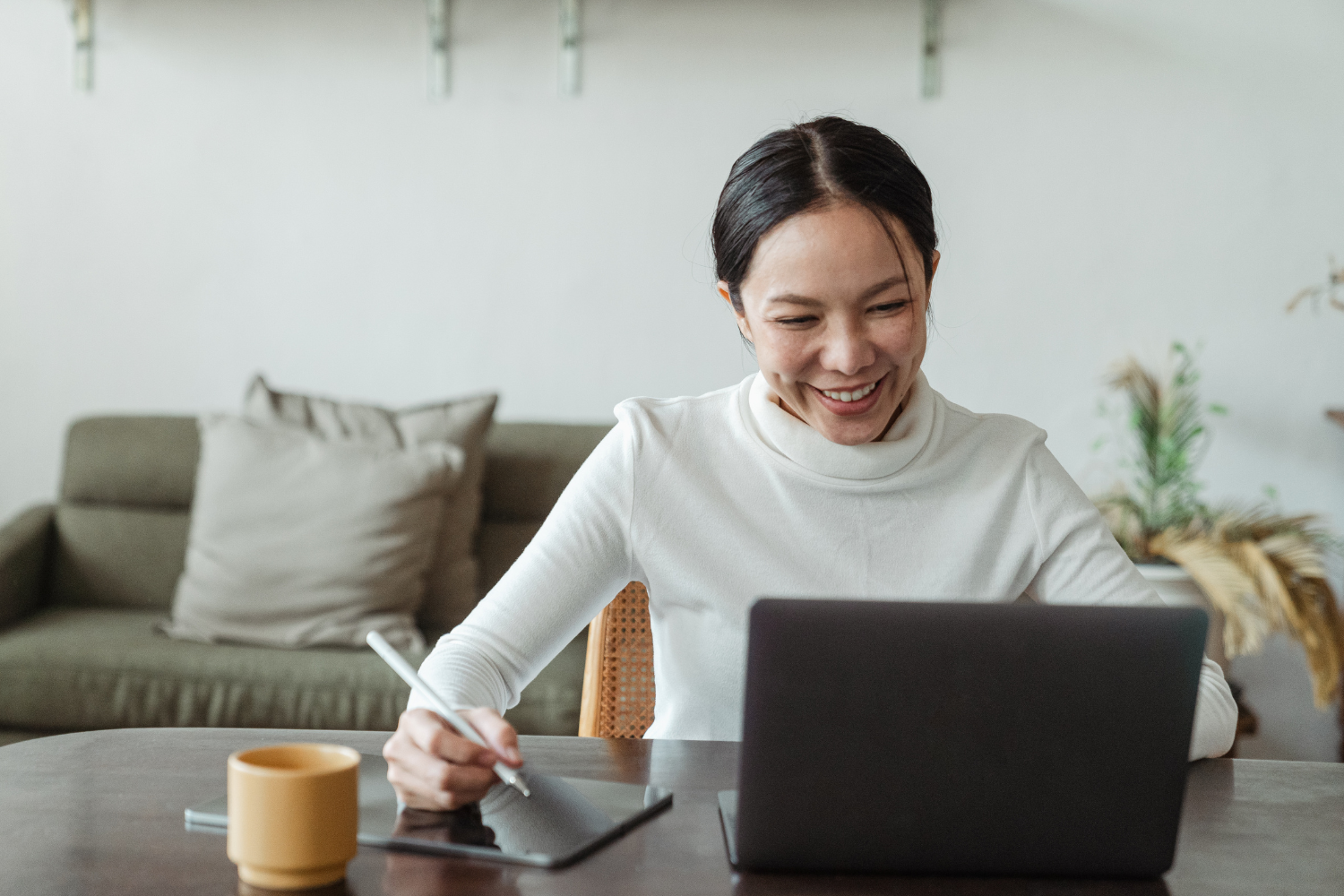 Smiling remote employee working on laptop while writing down notes.