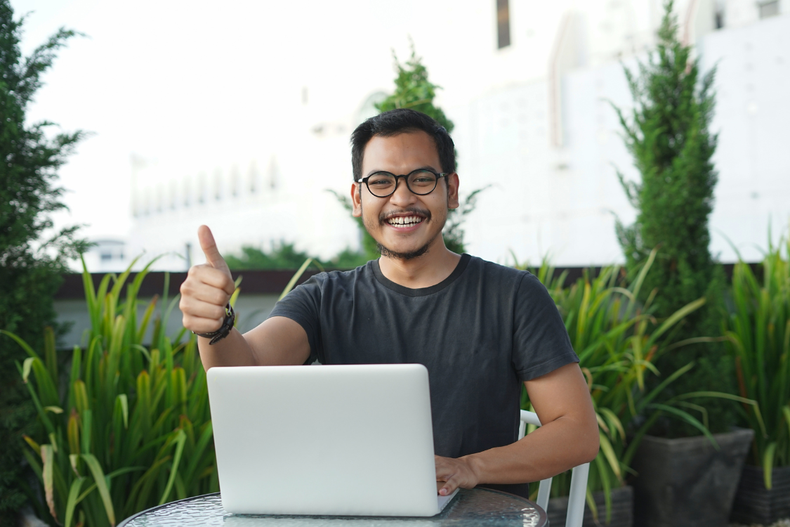Filipino remote worker giving a thumbs up outdoors, showing job satisfaction and positive team connection