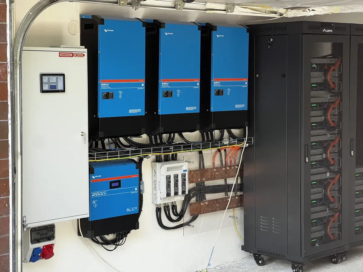 Na zdjęciu widoczny jest nowoczesny magazyn energii zamontowany w garażu obok falownika, który jest częścią instalacji fotowoltaicznych. Magazynowanie energii pozwala na efektywne wykorzystanie energii słonecznej w gospodarstwie domowym, zapewniając długoterminowe oszczędności i inteligentne zarządzanie energią. Panele, prąd, mocy, zapotrzebowanie technologii zwiększenie prosumentów.