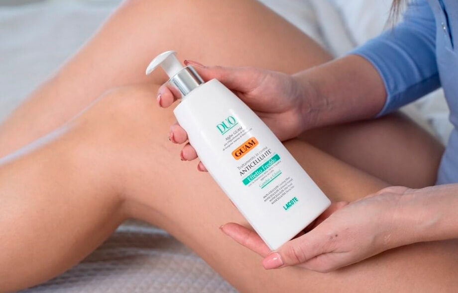 Donna che tiene fra me mani il flacone di trattamento anti-cellulite effetto freddo.