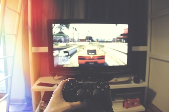 Person holding Playstation controller with racing game on TV