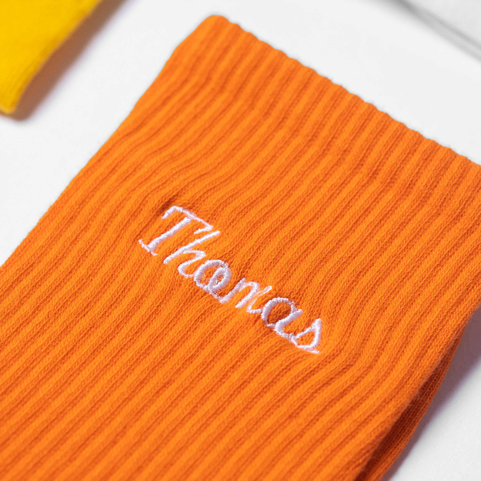 A flat-lay image of custom mens orange crew socks with the male name 'Thomas' embroidered in white thread.