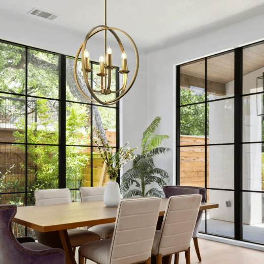 Elegant dining room with large black-framed windows, featuring a modern gold chandelier with candle-style lights hanging above a wooden dining table surrounded by upholstered chairs.