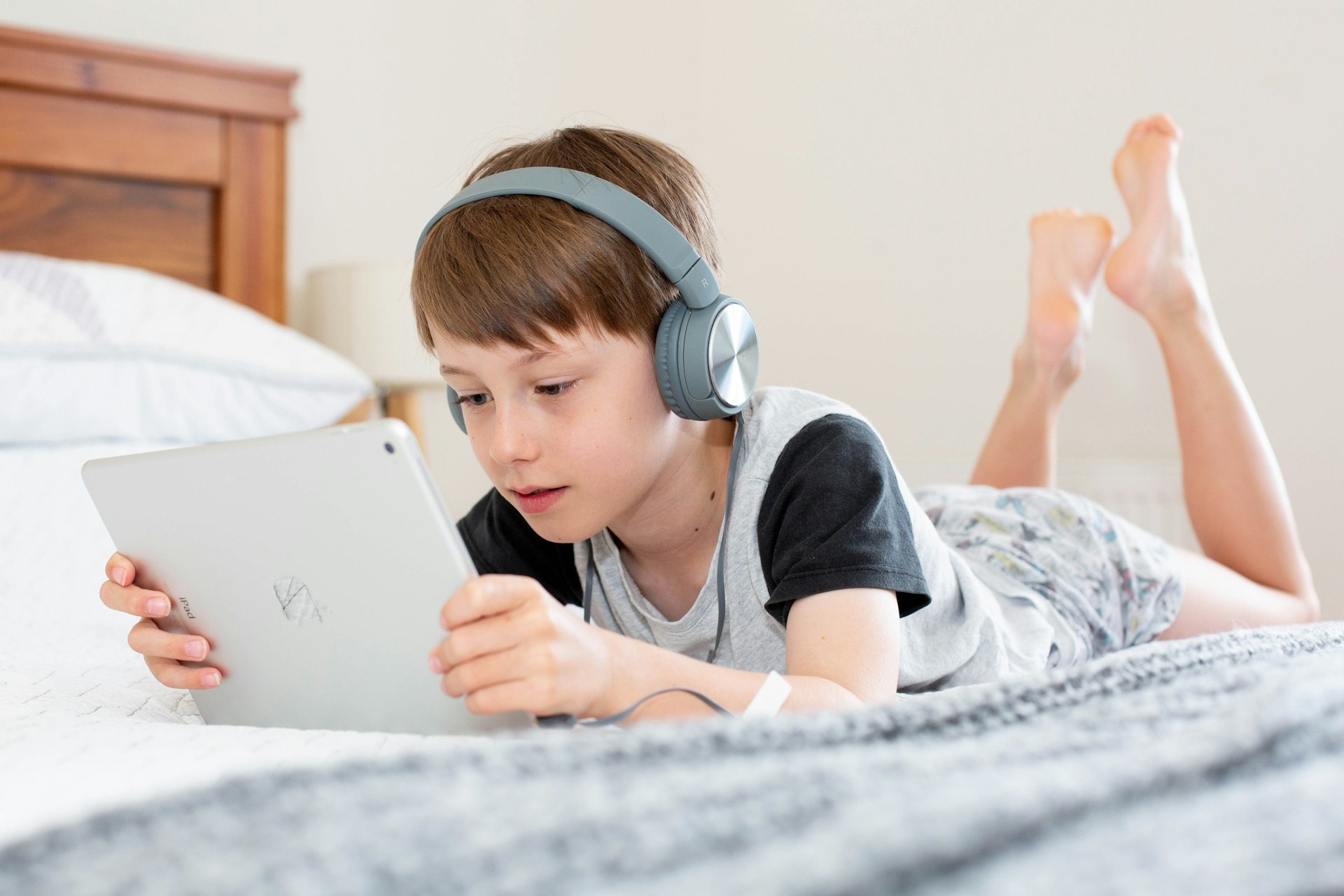young boy sitting on bed on an iPad with headphones on