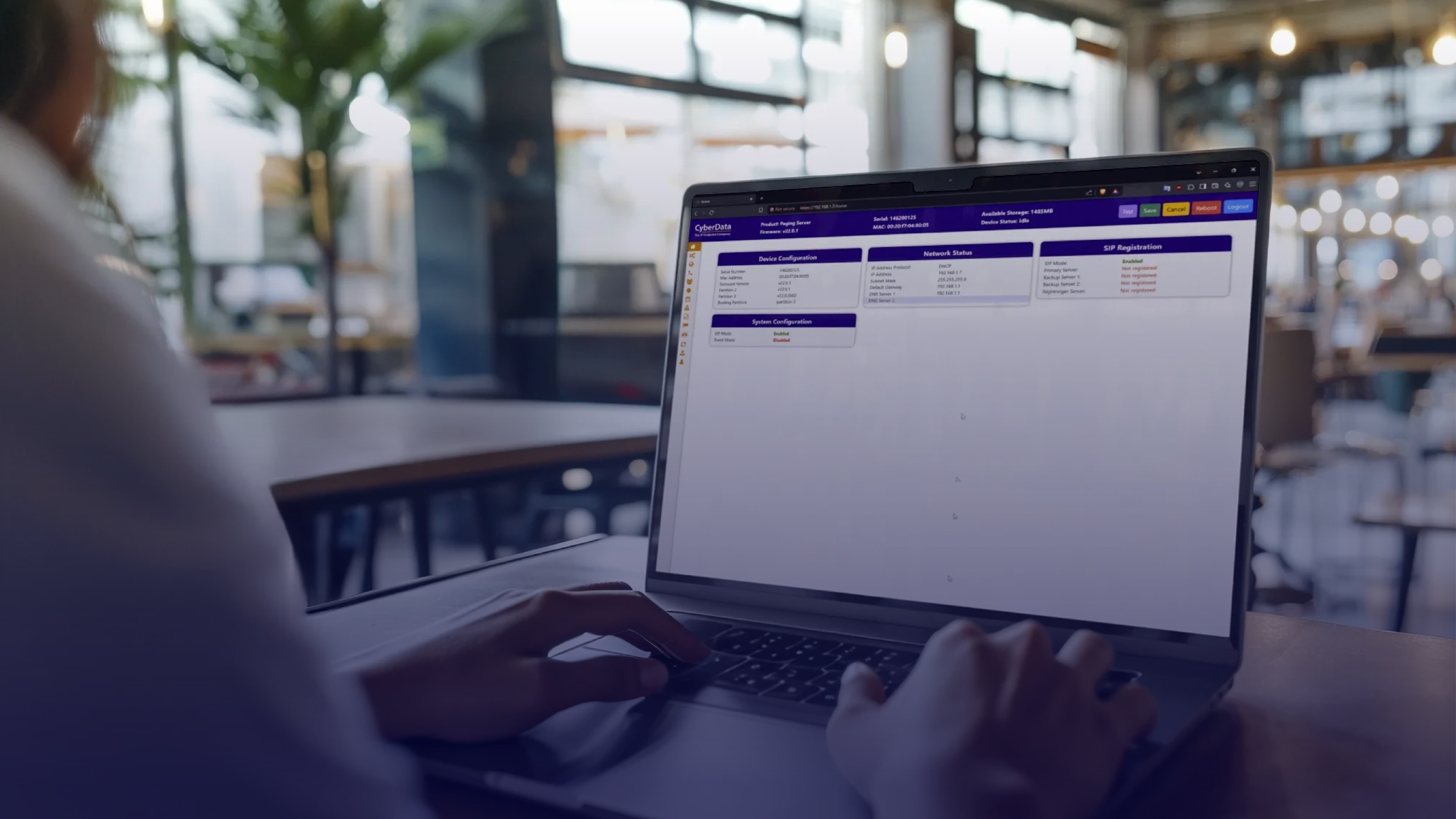 Person managing system configuration on a laptop in an open workspace, highlighting team communication and project management capabilities using CyberData’s control interface.