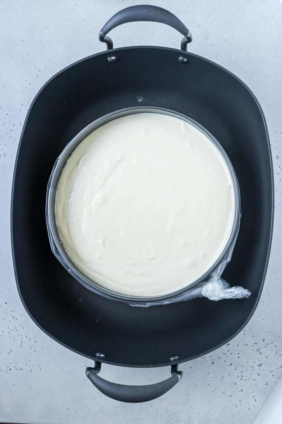 unbaked cheesecake placed inside large roasting pan