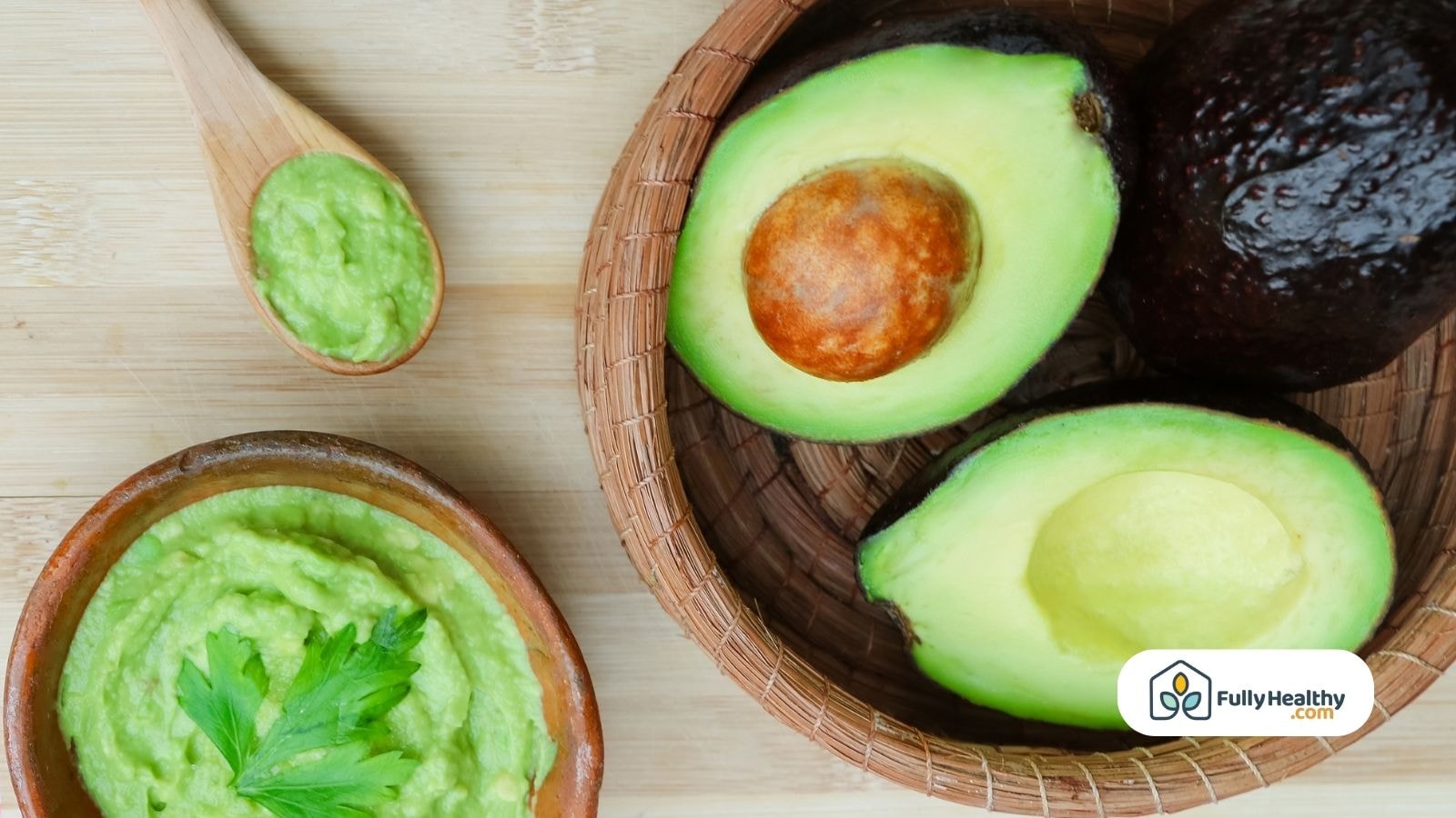 Fresh avocado halves and mashed avocado in wooden bowl