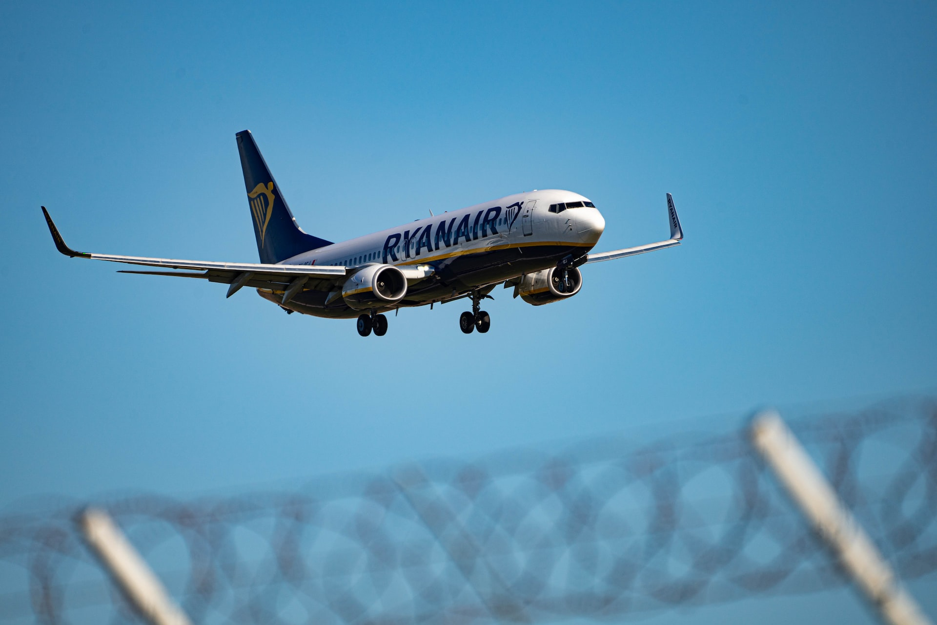 A Ryanair aircraft landing at an airport behind a barbed wire fence.