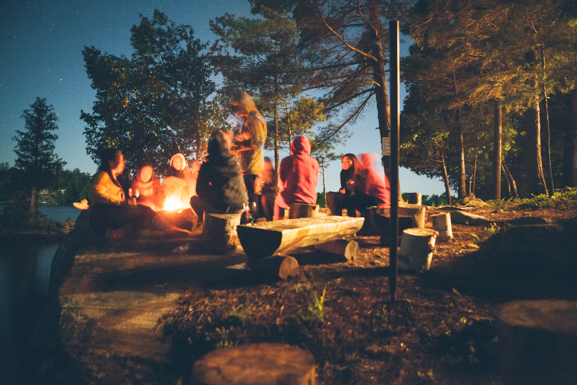 people sitting around a campfire at dusk in nature