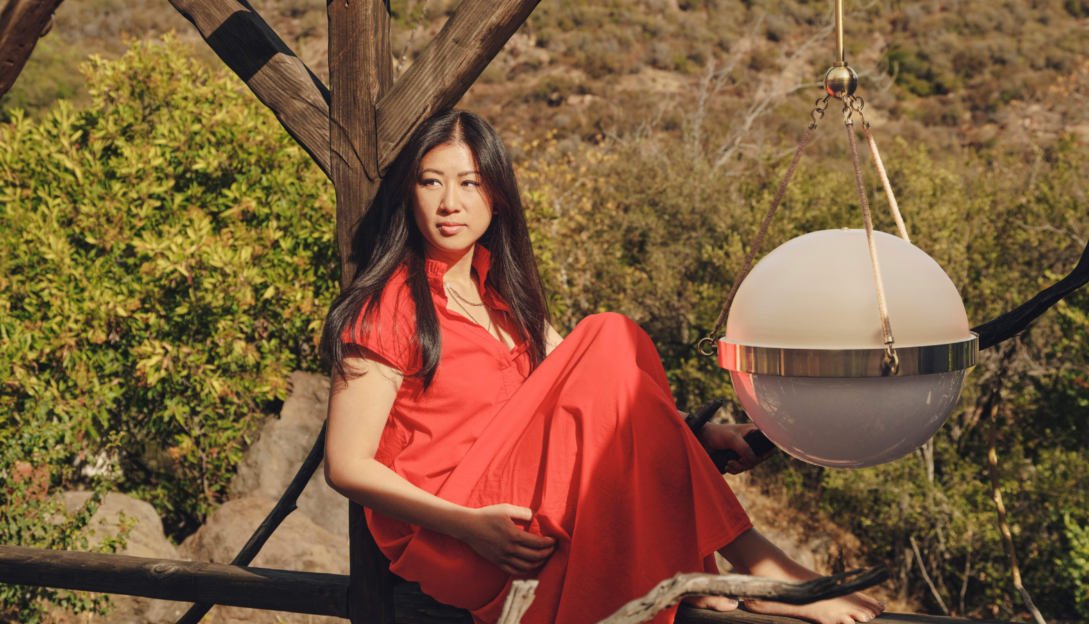 Mandy Cheng sitting outdoors beside a suspended globe pendant light from her Mitzi Tastemakers collection.
