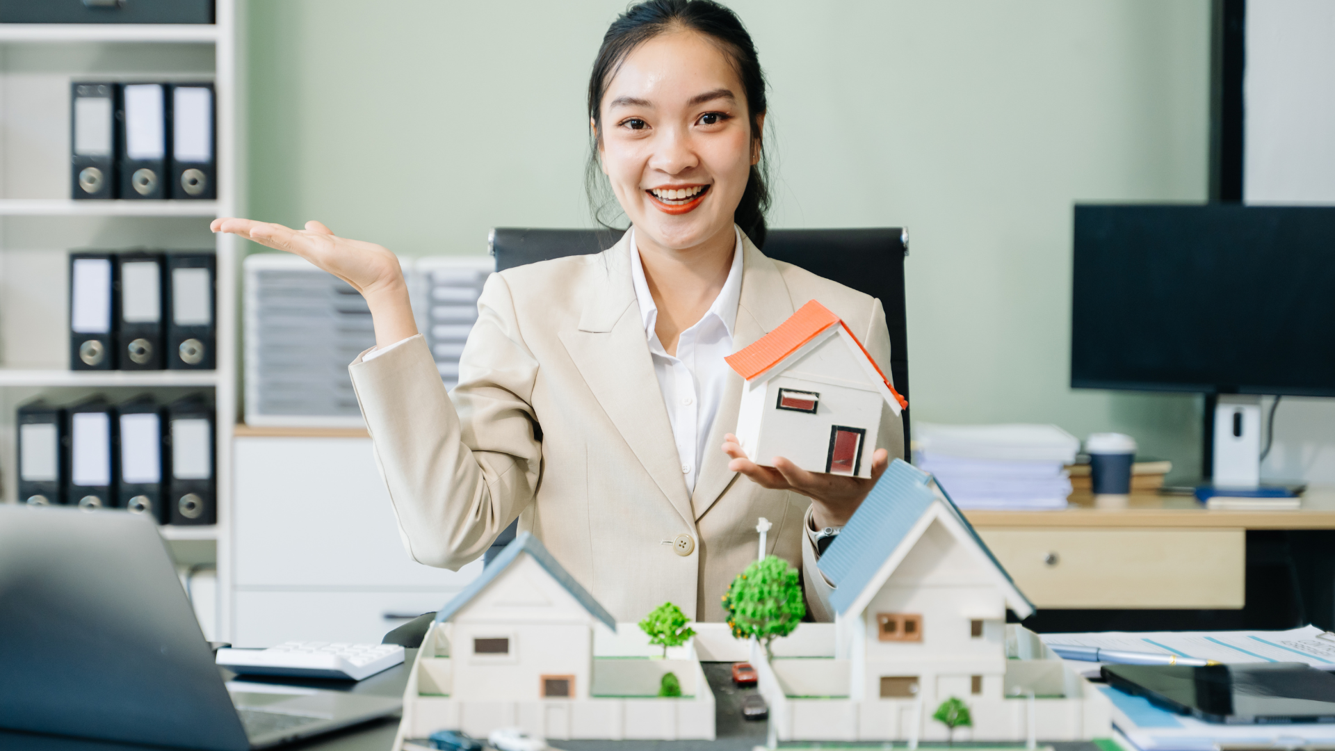Smiling property manager holding a model home while meeting with a landlord, illustrating signs it’s time to hire a property manager for rental property oversight and tenant management support.