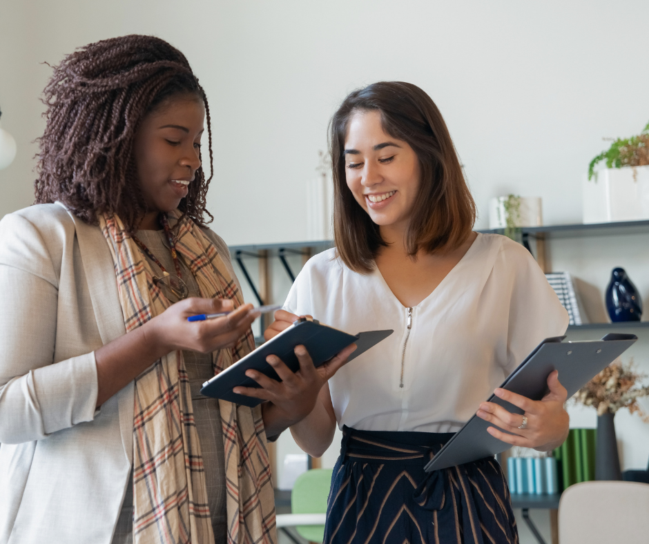 two women look at a tablet and clipboard