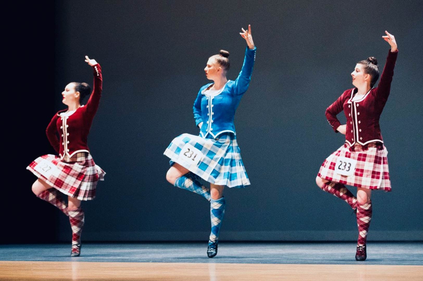 Performers showcasing Highland dance on stage in traditional plaid outfits.