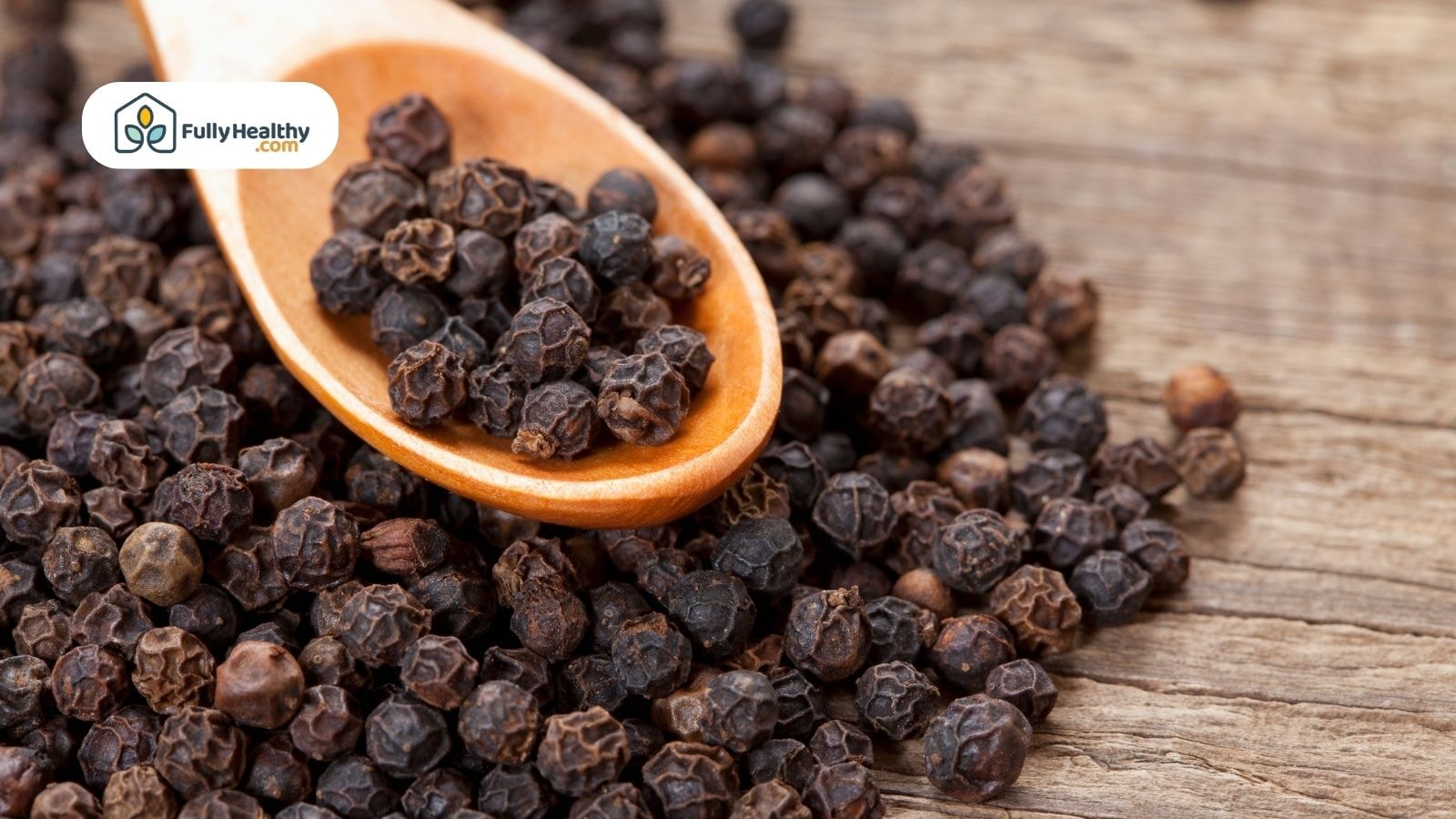 Wooden spoon filled with black peppercorns on wooden table