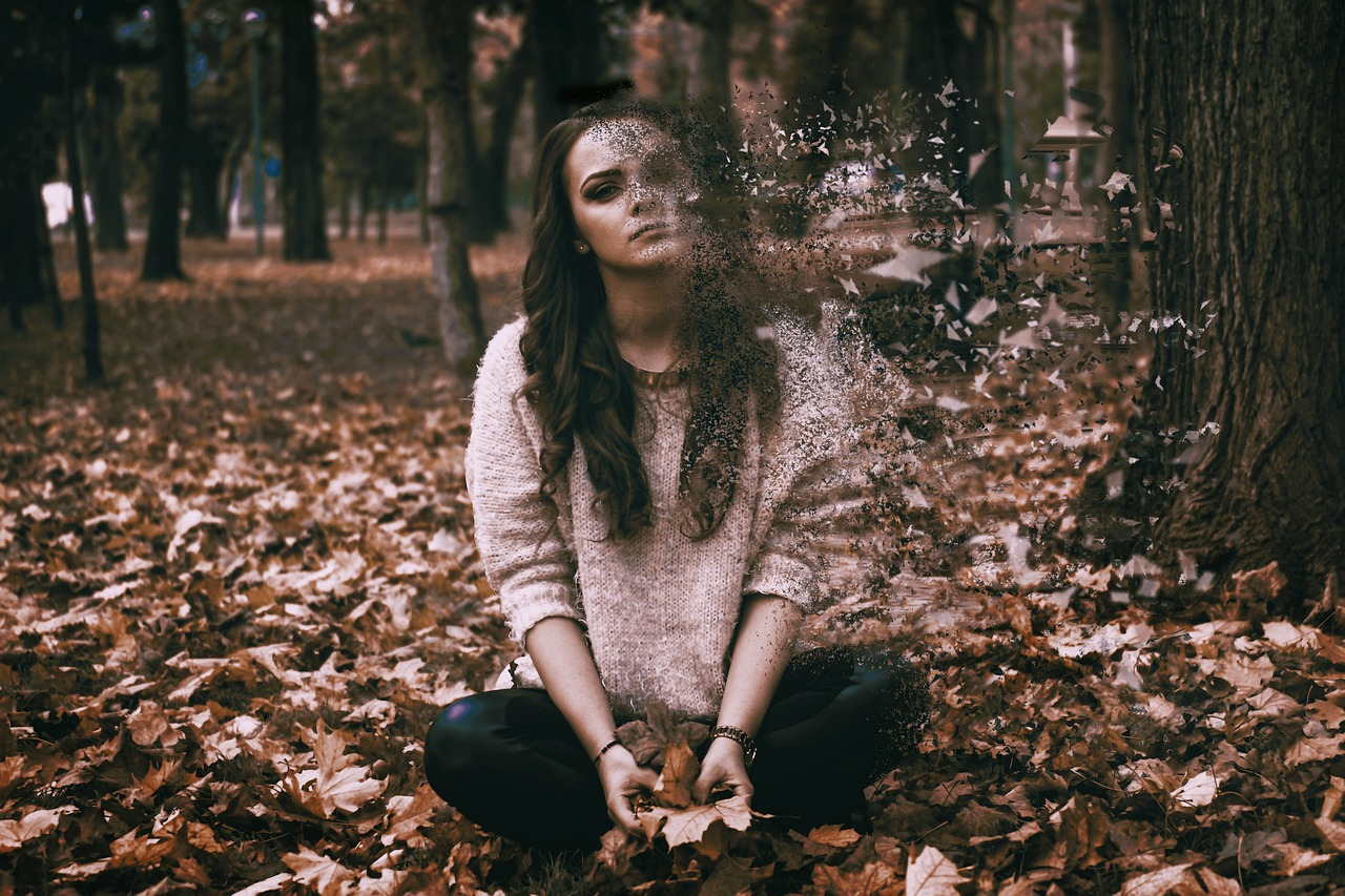 An image of a sad depressed young woman sitting in fall leaves outside.