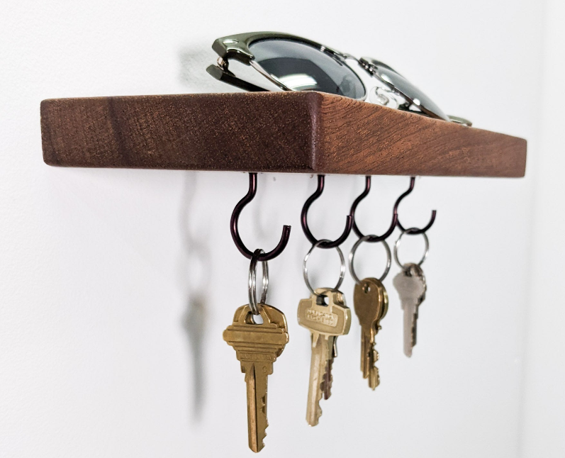 Four keys dangle from a mahogany floating shelf. A pair of black sunglasses rests on top 