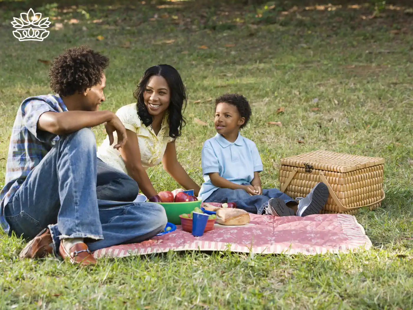 A family of three smiling and talking while enjoying a picnic with apples and sandwiches. Fabulous Flowers and Gifts - Picnic Gift Baskets Collection.