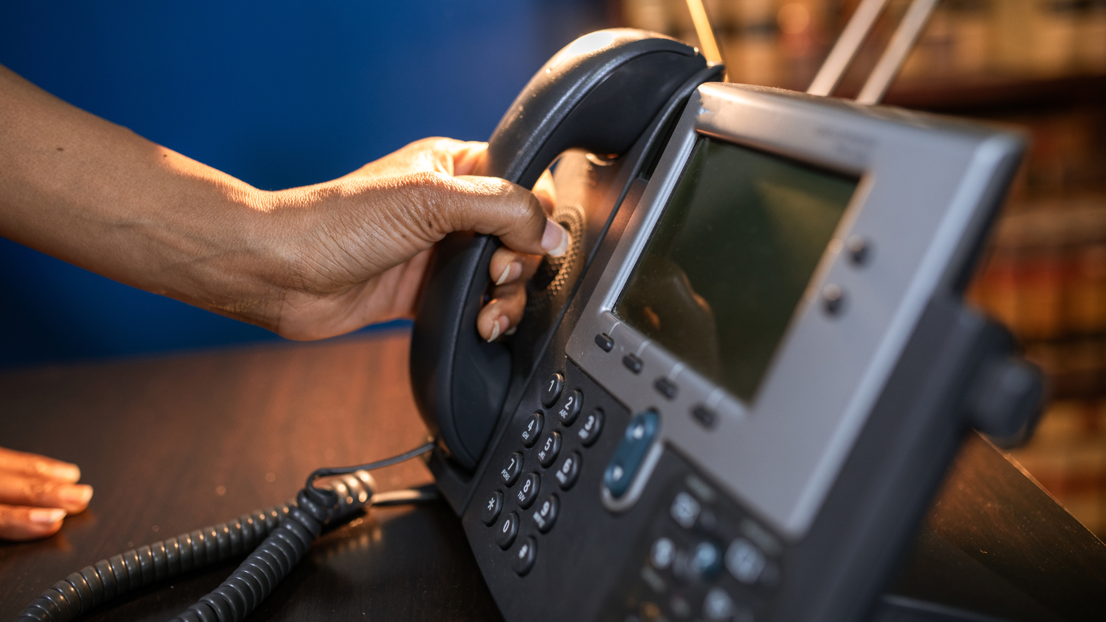 Hand picking up a desk phone receiver, symbolizing the standard plan for Victoria business phones: copper landlines.
