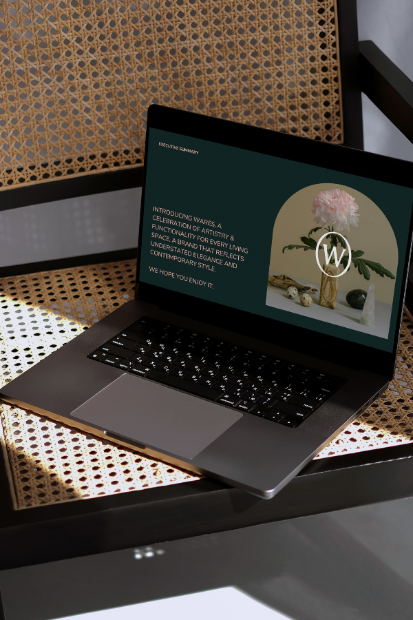 Laptop on cane chair displaying a brand presentation slide for Wares with text and floral graphic.