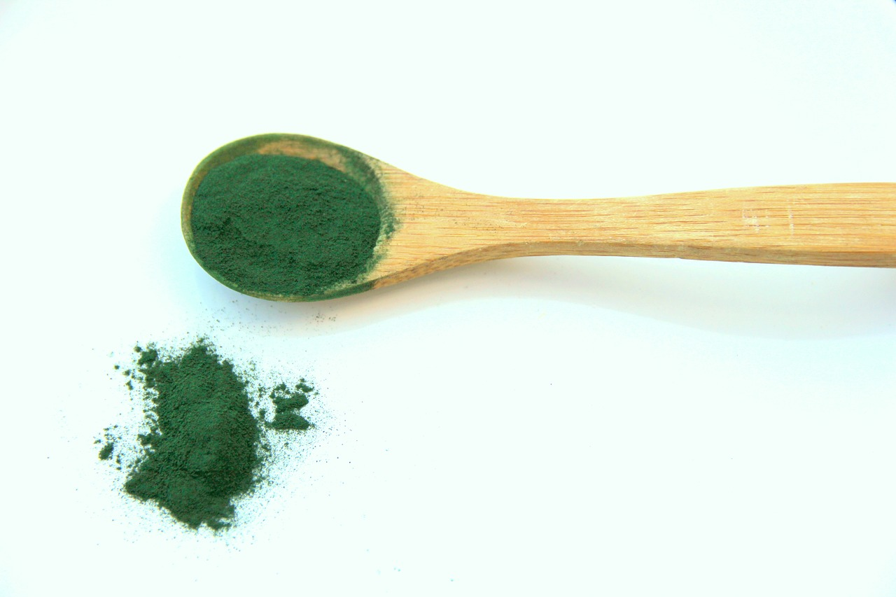 An image of spirulina powder in a wooden spoon and on the table.